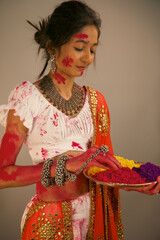 Beautiful young indian woman in traditional costume, holding powder colours in plate, celebrating holi festival.