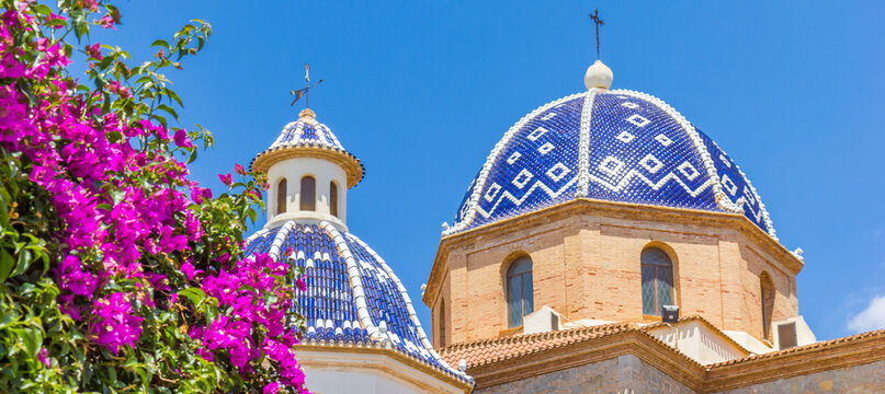 Panorama of purple flowers in front of the blue tiled dome of the church in Altea, Spain