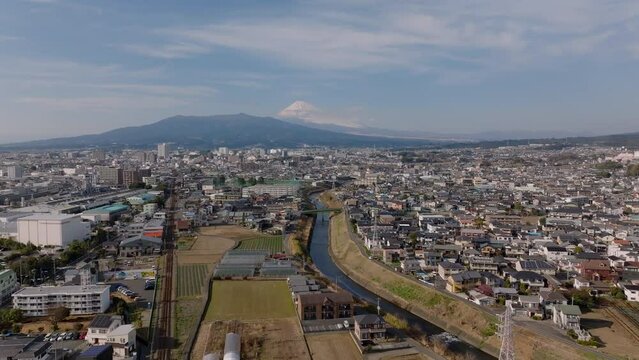 Aerial panoramic view of city with residential urban borough and Fujisan snowcapped mountain in distance. Descending footage. Japan