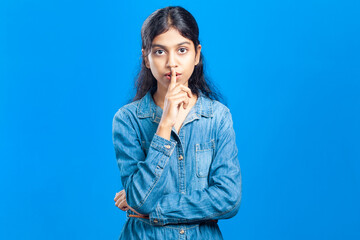 indian teenage girl showing shh gesture or silence gesture by touching finger on lips