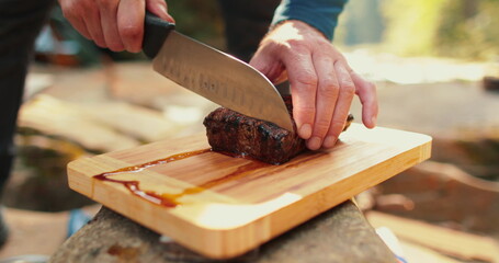 A man is slicing a juicy, freshly cooked steak outdoors. - obrazy, fototapety, plakaty