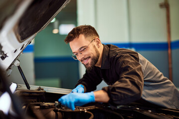 A smiling male mechanic technician checked a car under the opened hood, wearing protective gloves. - 761358030