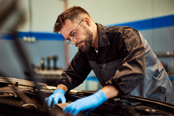 A hardworking mechanic man checking some car parts, working at his car repair shop. - 761358069