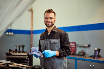 A smiling mechanic man posing for the camera, holding a tool for checking the oil in the car. - 761358094