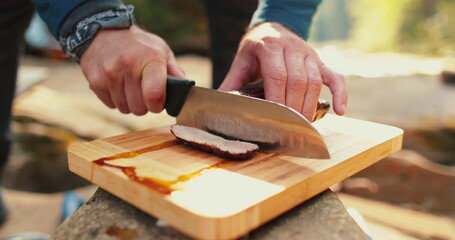 A man is slicing a juicy, freshly cooked steak outdoors. - obrazy, fototapety, plakaty