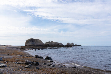 Fototapeta na wymiar A serene beach with large rocks in the water, a pebbly shore, under a sky with wispy clouds, evoking tranquility