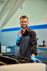 A mechanic working in his car repair service, holding a cloth, smiling for the camera. - 761358682