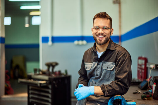 A smiling mechanic man is standing in his garage, posing for the camera. - Powered by Adobe