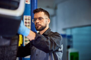 Fototapeta na wymiar A mechanic man working on a car fixing, holding a wheel, checking something.