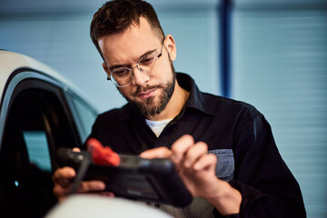 A focused mechanic man using a digital tablet, connected to a car with a cable, doing diagnostics. - 761359013