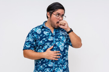 Adult male in a blue Hawaiian shirt clearing his throat or coughing, hand on chest, isolated on a white background. © Mdv Edwards