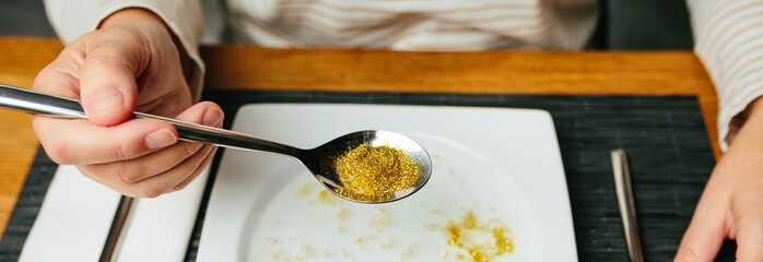 Banner of unrecognizable woman ready to eat holding a spoon full of golden glitter composed of...
