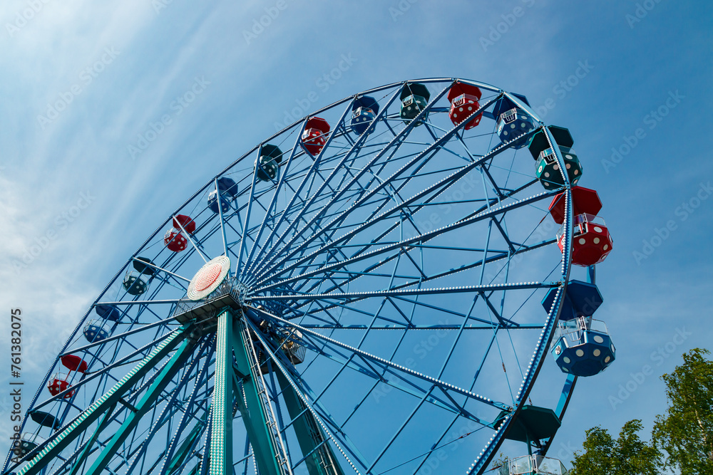 Wall mural Colorful ride ferris wheel in motion in amusement park on sky background.