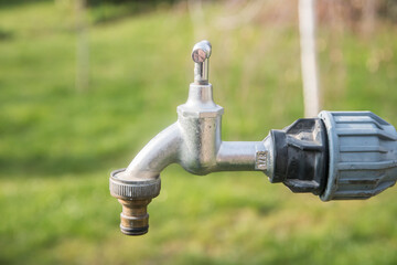 Water tap with metal garden hose adapter closeup on green grass background