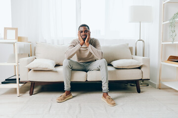 Young African American man sitting on a comfortable sofa in a modern living room He appears to be...