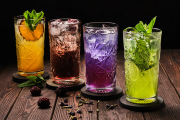 A variety of refreshing cocktails in different colors, garnished with fresh mint leaves, served on a rustic wooden table. - 761389620