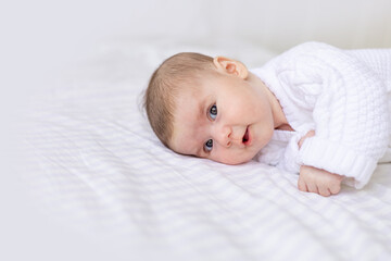 portrait of a newborn baby in a crib in a white warm jumpsuit on a white insulated cotton bed, cute...