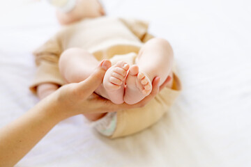 mom's hand holds the legs of a newborn baby in a crib on a white cotton bed
