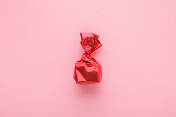 Candy wrapped in bright red foil paper on light pink table background. Pastel color. Closeup. Top...
