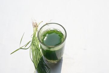 Wheatgrass juice on white background. Healthy organic green detox juice from grass of green germinated wheat grains. Healthy drink. Green leaves of young wheat and wheat grass juice.