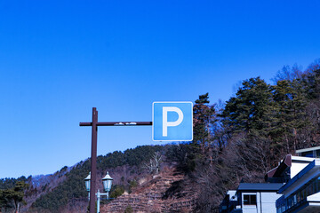 Parking (P) sign mounted on brown steel beam. Mountains, blue sky and bright sunlight in the background. Symbol aluminum white, blue post about Parking sign car showing free places. traffic sign - obrazy, fototapety, plakaty