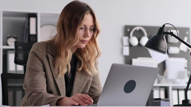 Focused Caucasian female freelancer typing on laptop, working in office. Texting and messaging, answering on work email, online communication concept.