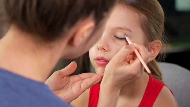 Mother applying makeup to her cute little daughter, close-up