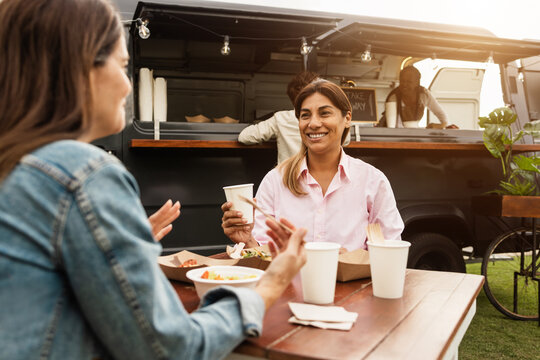 Multiracial people eating together in front of plastic free food truck outdoor - Women friends having fun eating dinner outside at summer time - Focus on latin female face