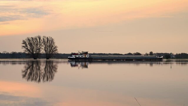 Ship sailing on the IJssel with winter light with high water level on the floodplains near Deventer after long periods of rain upstream. The overflown trees are reflected in the calm water.