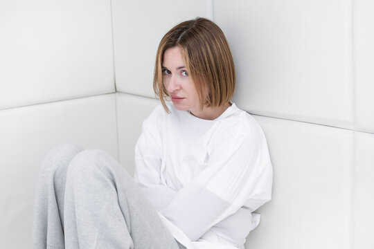 Young frustrated girl in a straitjacket is in an isolated white room in a mental hospital
