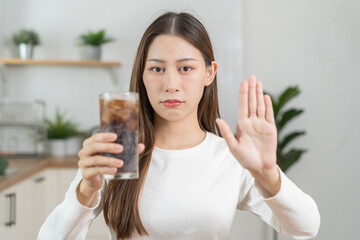 Diet, Dieting concept. Asian young woman, girl hand gesture push out, deny or refuse cola drink, sweet sparkling cold water on table in kitchen, eat food for good healthy, female getting weight loss.