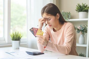 Financial owe, stressed asian woman, girl hand holding credit card, stressed by calculate expense from invoice or bill, no money to pay, mortgage or loan on table at home. Debt, bankruptcy or bankrupt