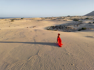 Elegant woman in red dress strolls through desert dunes