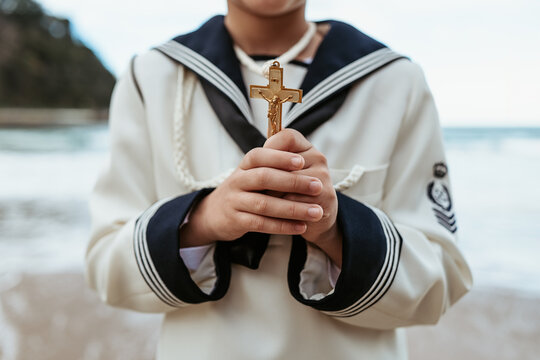 Focused image of anonymous child's hands reverently holding a golden crucifix during a First Communion ceremony by the sea