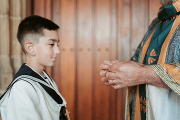 A young boy in First Communion attire looks on as anonymous priest prepares to give the blessing, a moment of faith and tradition