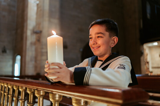 A thoughtful boy holds a lit candle during his First Communion, reflecting in a serene church setting