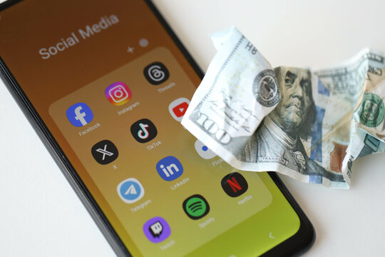 KYIV, UKRAINE - FEBRUARY 28, 2024 Social Media on smartphone display and crumpled dollar bill as concept of spend money to social networks and media services