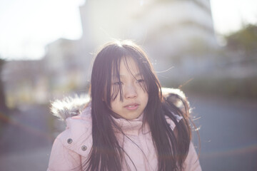 寒い風の中に住宅地にいる小学生の女の子の寒い顔の様子