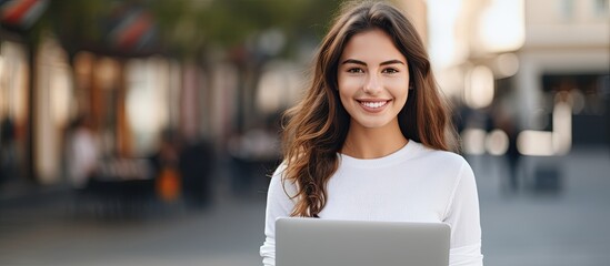 The woman is smiling while holding a laptop computer. Her face radiates happiness as she holds the personal computer between her sleeve and thigh during the event - obrazy, fototapety, plakaty