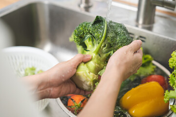 Close up asian young woman washing broccoli, tomato, carrot fresh vegetables, paprika with splash...