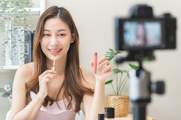 Cosmetic product, beauty blogger, asian young woman, girl vlogger makeup face, showing, review lip gloss while recording video, tutorial to share on social media. Business online influencer on camera.