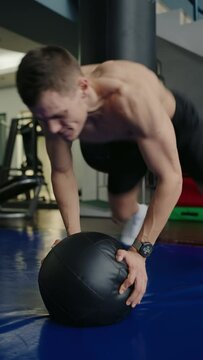 Sporty man exercising in gym with sport equipment, throw ball and push up. Young male with athletic body has functional training at fitness center. Vertical video
