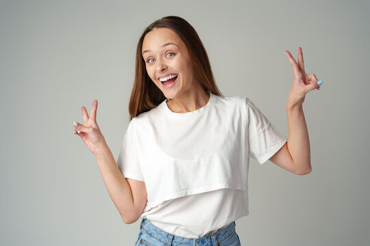 Smiling young woman showing victory sign on gray background