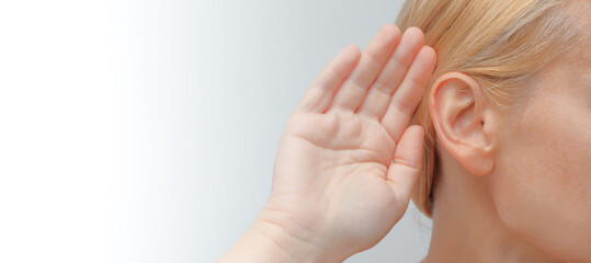 Lady with hearing aid put her hand to her ear. Young woman with hearing aid on light background.