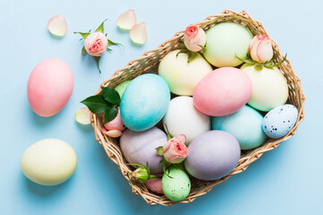 Happy Easter. Easter eggs in basket on colored table with yellow roses. Natural dyed colorful eggs background top view with copy space
