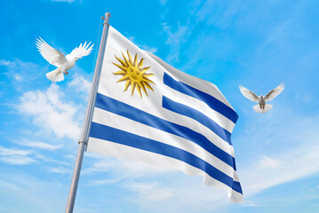 Waving flag of Uruguay in beautiful sky and flying pigeons. Uruguay flag for independence day. The symbol of the state on wavy fabric.
