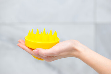 Yellow massage brush for hair growth stimulating brush in hand.