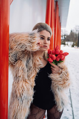 A girl in a bodysuit and a fur coat with flowers poses in different locations