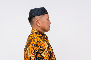 Side profile view of an Indonesian man in a colorful batik shirt and a black songkok against a white background.