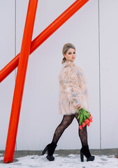 A girl in a bodysuit and a fur coat with flowers poses in different locations